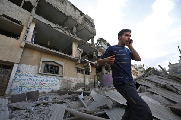  Palestinian talks on a mobile phone as he walks on the rubble of a damaged house following an overnight Israeli missile strike in Gaza City, Tuesday, July 15, 2014 - Sputnik International