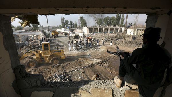 An Afghan policeman keeps watch while men gather at the site of a suicide car bomb attack in Surkhrod district of Nangarhar province, Afghanistan, December 7, 2015 - Sputnik International