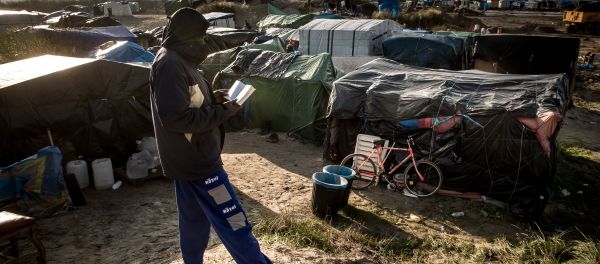 A man walks past a banner reading Pray for Deir Ezzor at the migrant camp known as the Jungle in Calais on December 7, 2015 - Sputnik International