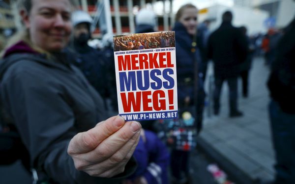 A supporter of the anti-immigration right-wing movement PEGIDA (Patriotic Europeans Against the Islamisation of the West) holds up a sticker for a photo during a demonstration rally in Cologne, Germany January 9, 2016. The sticker reads, Merkel must go! - Sputnik International
