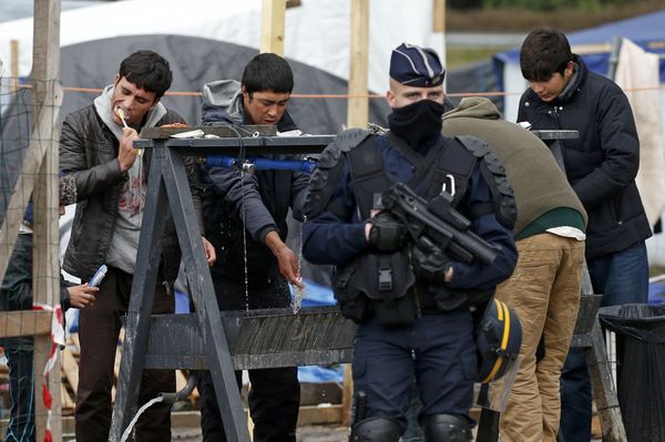 A French riot police officer (CRS) stands guard as migrants brush their teeth in a makeshift camp in what is known as the Jungle, a squalid sprawling camp in Calais, northern France, January 11, 2016. A French riot police officer (CRS) stands guard as migrants brush their teeth in a makeshift camp in what is known as the Jungle, a squalid sprawling camp in Calais, northern France, January 11, 2016. - Sputnik International