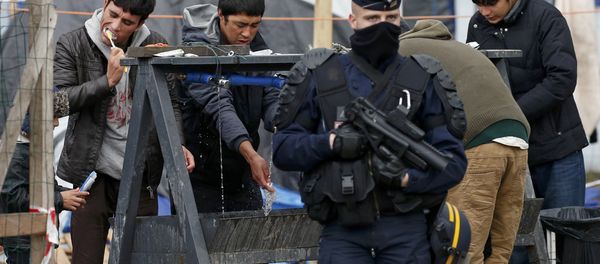 A French riot police officer (CRS) stands guard as migrants brush their teeth in a makeshift camp in what is known as the Jungle, a squalid sprawling camp in Calais, northern France, January 11, 2016. A French riot police officer (CRS) stands guard as migrants brush their teeth in a makeshift camp in what is known as the Jungle, a squalid sprawling camp in Calais, northern France, January 11, 2016. - Sputnik International