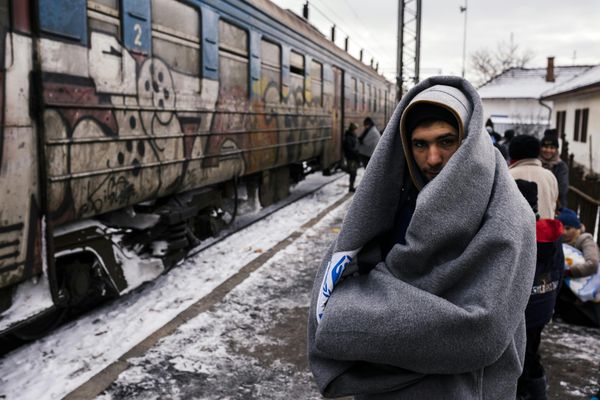 A migrant wrapped in a blanket to keep warm, waits with other migrants and refugees to board a train heading to the border with Croatia at the train station in Presevo, on January 19, 2016, after crossing the Macedonian border into Serbia - Sputnik International