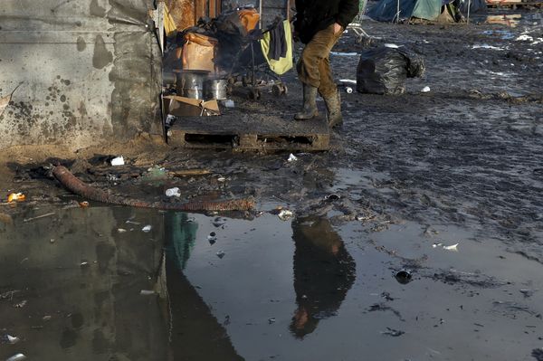 A migrant is reflected in a puddle as he walks past shelters in a muddy field called the Grande-Synthe jungle, near Dunkirk, northern France - Sputnik International