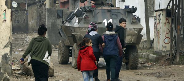 Backdropped by a Turkish forces armoured personnel carrier, residents walk around after the 24-hour curfew was lifted, in the mostly-Kurdish town of Silopi, in southeastern Turkey, near the border with Iraq, Tuesday, Jan. 19, 2016 - Sputnik International