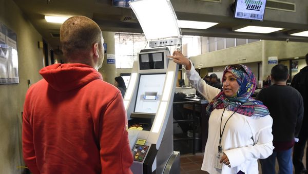 Contractor Sabira Dewji, right, helps a pedestrian crossing from Mexico into the United States at the Otay Mesa Port of Entry have his facial features and eyes scanned at a biometric kiosk Thursday, Dec. 10, 2015, in San Diego - Sputnik International