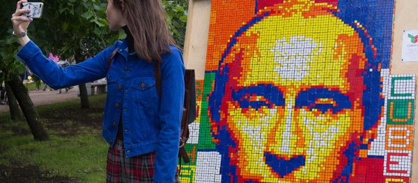A girl takes a selfie against a portrait of Russian President Vladimir Putin composed of Rubik's Cubes at the festival of the social network VKontakte in St. Petersburg - Sputnik International
