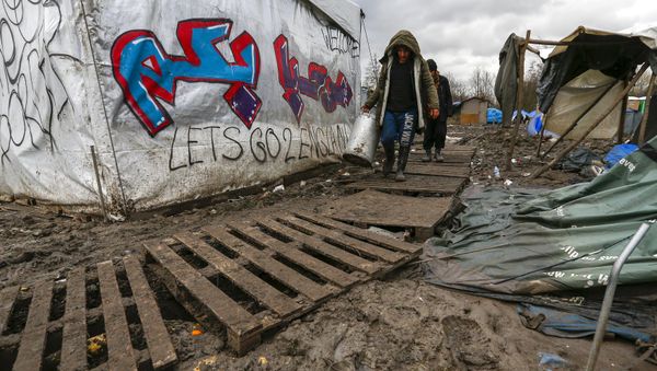 Migrants walk among tents in a muddy field at a camp of makeshift shelters for migrants and asylum-seekers from Iraq, Kurdistan, Iran and Syria, called the Grande Synthe jungle, near Calais, France - Sputnik International