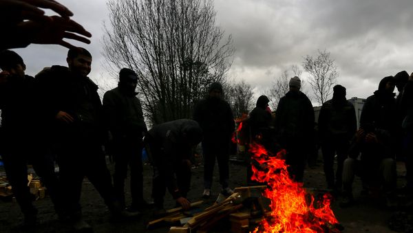 Migrants try to warm up around a brazier in a muddy field at a camp of makeshift shelters. Migrants try to warm up around a brazier in a muddy field at a camp of makeshift shelters. - Sputnik International