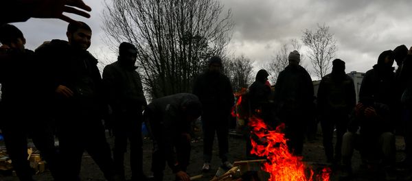 Migrants try to warm up around a brazier in a muddy field at a camp of makeshift shelters. - Sputnik International