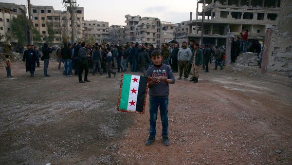 A boy carries an opposition flag as rebel fighters and civilians gather during the arrival of an aid convoy of Syrian Arab Red Crescent and United Nation (UN) to the rebel held besieged town of Kafr Batna, on the outskirts of Damascus, Syria February 23, 2016 - Sputnik International