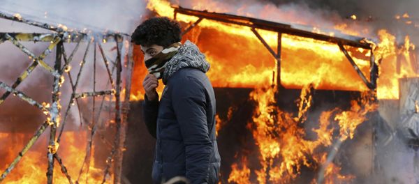 A migrant walks past a burning makeshift shelter set ablaze in protest against the partial dismantlement of the camp for migrants. A migrant walks past a burning makeshift shelter set ablaze in protest against the partial dismantlement of the camp for migrants. - Sputnik International