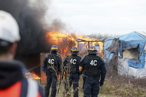 French CRS riot police watch as smoke and flames billow from a burning makeshift shelter. - Sputnik International