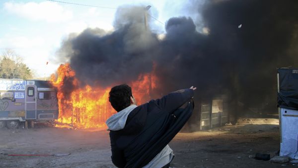 A youth throws a stone as smoke and flames rise from a burning makeshift shelter in protest against the partial dismantlement of the camp for migrants called the jungle, in Calais, northern France, February 29, 2016. - Sputnik International