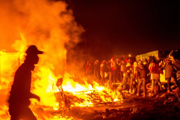 Migrants stand next a fire burning shacks, in the southern part of the so-called Jungle migrant camp, as half of the camp is being dismantled, in the French northern port city of Calais, on March 1, 2016. Migrants stand next a fire burning shacks, in the southern part of the so-called Jungle migrant camp, as half of the camp is being dismantled, in the French northern port city of Calais, on March 1, 2016. - Sputnik International