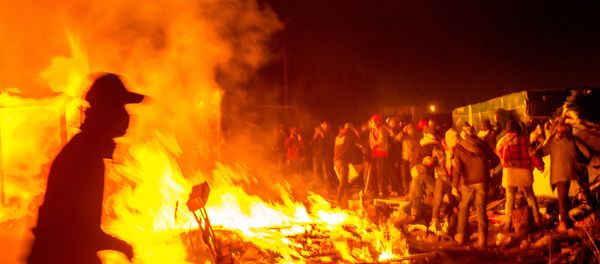 Migrants stand next a fire burning shacks, in the southern part of the so-called Jungle migrant camp, as half of the camp is being dismantled, in the French northern port city of Calais, on March 1, 2016. - Sputnik International