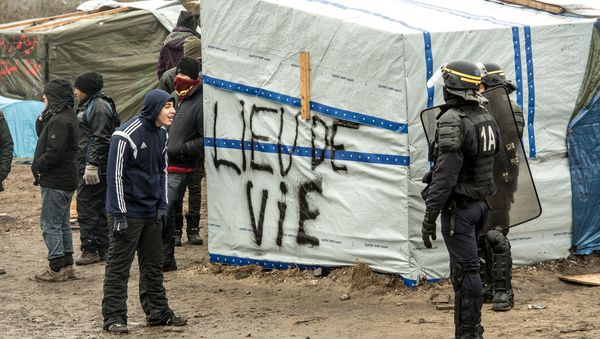 A migrant (L) talks to an anti-riot policeman during the dismantling of half of the Jungle migrant camp in the French northern port city of Calais, on March 1, 2016. A migrant (L) talks to an anti-riot policeman during the dismantling of half of the Jungle migrant camp in the French northern port city of Calais, on March 1, 2016. - Sputnik International