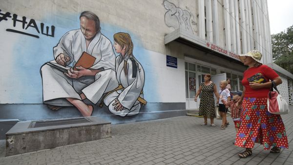 Women with children walk past graffiti showing Russian President Vladimir Putin, dressed in a Judogi and sitting next to a girl, on the front of a children's clinic in Yalta, Crimea, Wednesday, Aug. 19, 2015 Women with children walk past graffiti showing Russian President Vladimir Putin, dressed in a Judogi and sitting next to a girl, on the front of a children's clinic in Yalta, Crimea, Wednesday, Aug. 19, 2015 - Sputnik International
