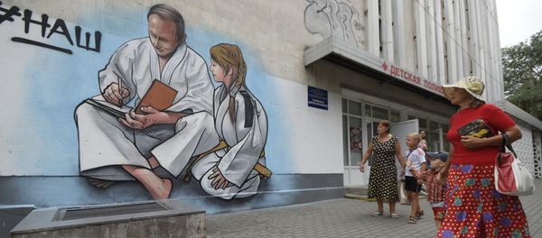 Women with children walk past graffiti showing Russian President Vladimir Putin, dressed in a Judogi and sitting next to a girl, on the front of a children's clinic in Yalta, Crimea, Wednesday, Aug. 19, 2015 Women with children walk past graffiti showing Russian President Vladimir Putin, dressed in a Judogi and sitting next to a girl, on the front of a children's clinic in Yalta, Crimea, Wednesday, Aug. 19, 2015 - Sputnik International