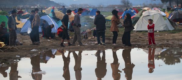 Migrants are reflected in a puddle at the northern Greek border station of Idomeni, Tuesday, March 8, 2016. - Sputnik International