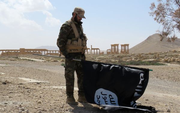 A member of the Syrian pro-government forces carries an Islamic State (IS) group flag as he stands on a street in the ancient city of Palmyra on March 27, 2016, after troops recaptured the city from IS jihadists - Sputnik International