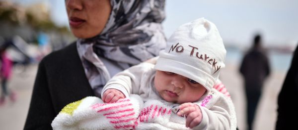 A Syrian refugee holds a two-month old baby as refugees and migrants who broke out from Chios detention camp, and camped out in the port of the city, stage a protest with their children chanting 'No Turkey' on April 3, 2016. A Syrian refugee holds a two-month old baby as refugees and migrants who broke out from Chios detention camp, and camped out in the port of the city, stage a protest with their children chanting 'No Turkey' on April 3, 2016. - Sputnik International
