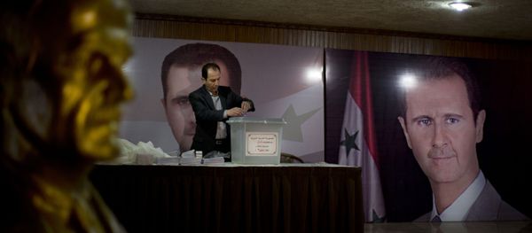 A Syrian election official waits for voters at a polling station with posters of President Bashar Assad during the parliamentary election in Damascus, Syria - Sputnik International