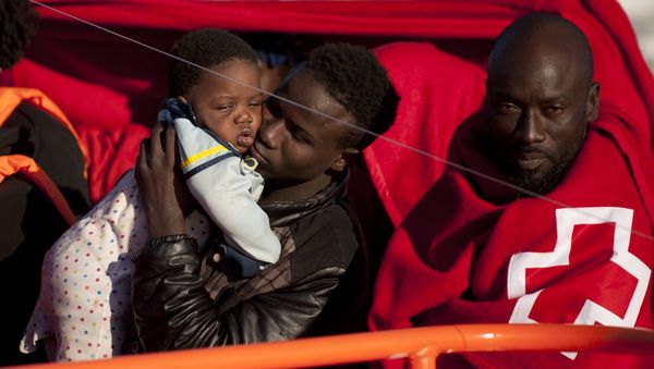 A migrants wrapped in a red cross blanket holds a child on arrival into the southern Spanish port of Malaga on January 27, 2016 after an inflatable boat carrying 55 Africans, seven of them women and six chidren, was rescued by the Spanish coast guard off the Spanish coast (File) A migrants wrapped in a red cross blanket holds a child on arrival into the southern Spanish port of Malaga on January 27, 2016 after an inflatable boat carrying 55 Africans, seven of them women and six chidren, was rescued by the Spanish coast guard off the Spanish coast (File) - Sputnik International