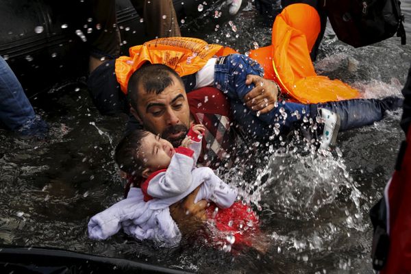 A Syrian refugee holds onto his children as he struggles to walk off a dinghy on the Greek island of Lesbos, after crossing a part of the Aegean Sea from Turkey to Lesbos. file photo  - Sputnik International