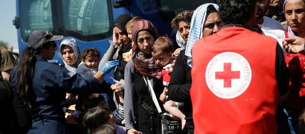 A woman holds two children as refugees and migrants wait to board a bus that will transfer them from a makeshift camp at the port of Piraeus to a newly built relocation centre in the port town of Skaramagkas, in western Athens, Greece April 18, 2016 A woman holds two children as refugees and migrants wait to board a bus that will transfer them from a makeshift camp at the port of Piraeus to a newly built relocation centre in the port town of Skaramagkas, in western Athens, Greece April 18, 2016 - Sputnik International