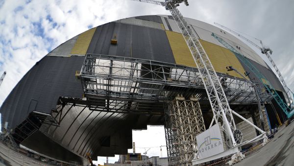 Workers walk man machinery in front of the shelter and containment area built over the destroyed fourth block of the Chernobyl nuclear power plant as they work on the construction of the New Safe Confinement structure (NSC) near Pripyat on April 16, 2016 - Sputnik International