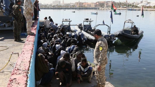 Illegal migrants sit on the dock at the Tripoli port after 115 migrants of African origins were rescued by two coast guard boats at sea when their boat started sinking off the Libyan coast on April 11, 2016 - Sputnik International