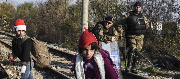Police officers watch two children walk past as migrants and refugees cross the Greek-Macedonian border near the town of Gevgelija, Macedonia (File) Police officers watch two children walk past as migrants and refugees cross the Greek-Macedonian border near the town of Gevgelija, Macedonia (File) - Sputnik International
