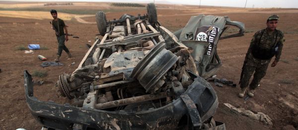 Peshmerga fighters inspect the remains of a car, bearing an image of the trademark jihadist flag, which reportedly belonged to Islamic State (IS) militants after it was targeted by an American air strike in the village of Baqufa, north of Mosul (File) - Sputnik International