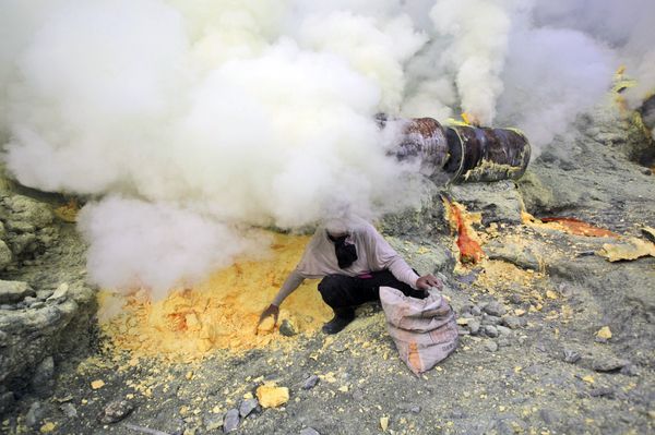 In this April 16, 2016 photo, volcanic smoke blankets a miner as he collects sulfur rocks he just dug up at the crater of Mount Ijen in Banyuwangi, East Java, Indonesia - Sputnik International