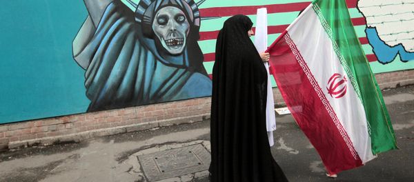 An Iranian woman holds her national flag as she walks past an anti-US mural depicting the Statue of Liberty on the wall of the former US embassy in Tehran (File) - Sputnik International