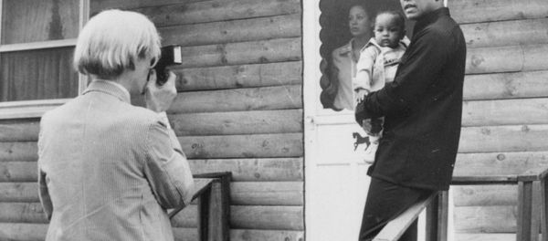 Pop artist Andy Warhol, left, is shown photographing Muhammad Ali, his infant daughter, Hanna, and wife, Veronica, Thursday, August 18, 1977, at Ali's training camp in Deer Lake, Pa. - Sputnik International