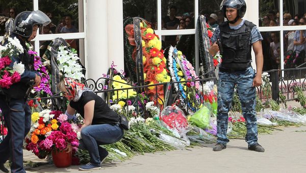A woman places flowers as Interior Ministry members stand guard outside the firearms shop, which was a target of a recent suspected Islamist militant attack, during the funeral of salesman Andrey Maksimenko in Aktobe, Kazakhstan, June 8, 2016 - Sputnik International