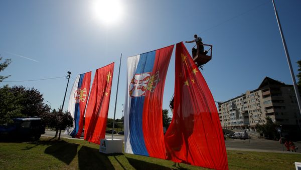 A worker adjusts Chinese and Serbian flags for the upcoming visit of Chinese President Xi Jinping - Sputnik International