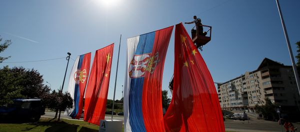 A worker adjusts Chinese and Serbian flags for the upcoming visit of Chinese President Xi Jinping - Sputnik International