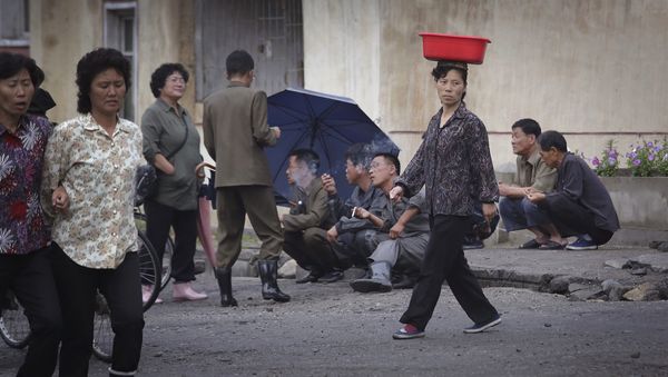 A North Korean woman balances a pail on her head while she walks past men smoking by the road at the end of a work day on Wednesday, June 22, 2016, in Wonsan, North Korea. - Sputnik International