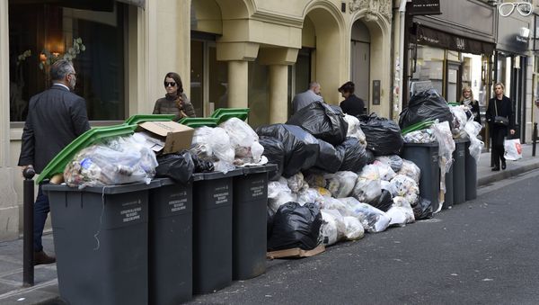 Pedestrians walk past unemptied garbage bins and plastic bags during a strike of garbage collectors in a street in Paris (File) - Sputnik International