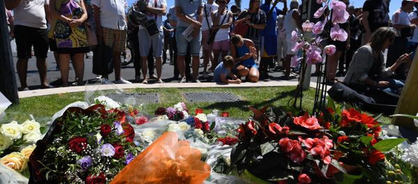 People stand on July 15, 2016 in front of flowers and candles placed near the site in Nice where a gunman smashed a truck into a crowd of revellers celebrating Bastille Day, killing at least 84 people. - Sputnik International