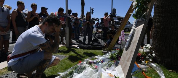 A man kneels and holds his head on July 15, 2016 in front of flowers placed near the site in Nice where a gunman smashed a truck into a crowd of revellers celebrating Bastille Day, killing at least 84 people. - Sputnik International
