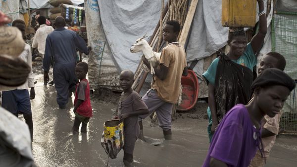 South-Sudanese man carries a goat as he and others wade through mud-filled paths between makeshift tents in the United Nations base (File) - Sputnik International