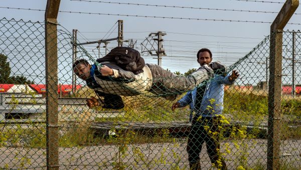 A migrant climbs over a fence in Coquelles, near Calais northern France - Sputnik International