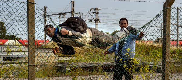 A migrant climbs over a fence in Coquelles, near Calais northern France A migrant climbs over a fence in Coquelles, near Calais northern France - Sputnik International