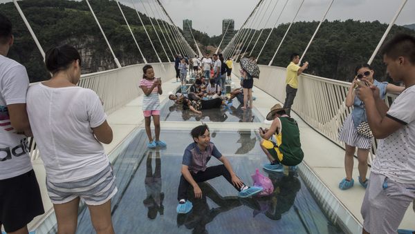 A tourist poses for a photograph on the world's highest and longest glass-bottomed bridge above a valley in Zhangjiajie in China's Hunan Province on August 20, 2016 A tourist poses for a photograph on the world's highest and longest glass-bottomed bridge above a valley in Zhangjiajie in China's Hunan Province on August 20, 2016 - Sputnik International
