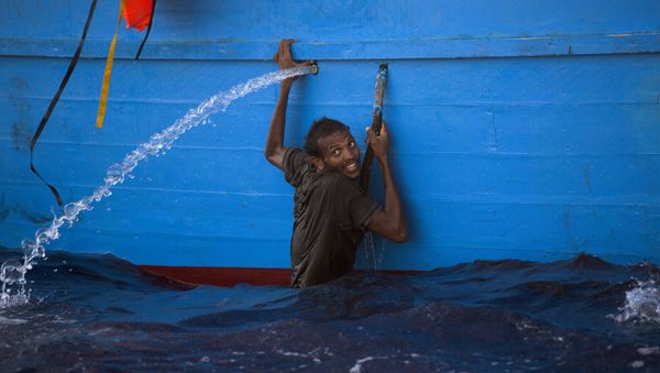 A man holds himself on the side of a boat after jumping into the sea from a crowded wooden boat during a rescue operation at the Mediterranean sea, about 13 miles north of Sabratha, Libya, Monday, Aug. 29, 2016. A man holds himself on the side of a boat after jumping into the sea from a crowded wooden boat during a rescue operation at the Mediterranean sea, about 13 miles north of Sabratha, Libya, Monday, Aug. 29, 2016. - Sputnik International
