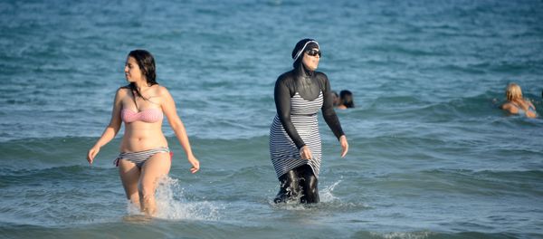 Tunisian women, one (R) wearing a burkini, a full-body swimsuit designed for Muslim women, swim at Ghar El Melh beach near Bizerte, north-east of the capital Tunis - Sputnik International